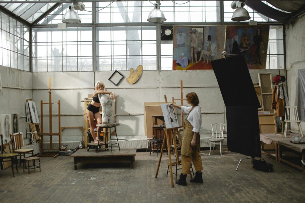 Art studio scene featuring an artist drawing a live model on an easel, showcasing creativity.