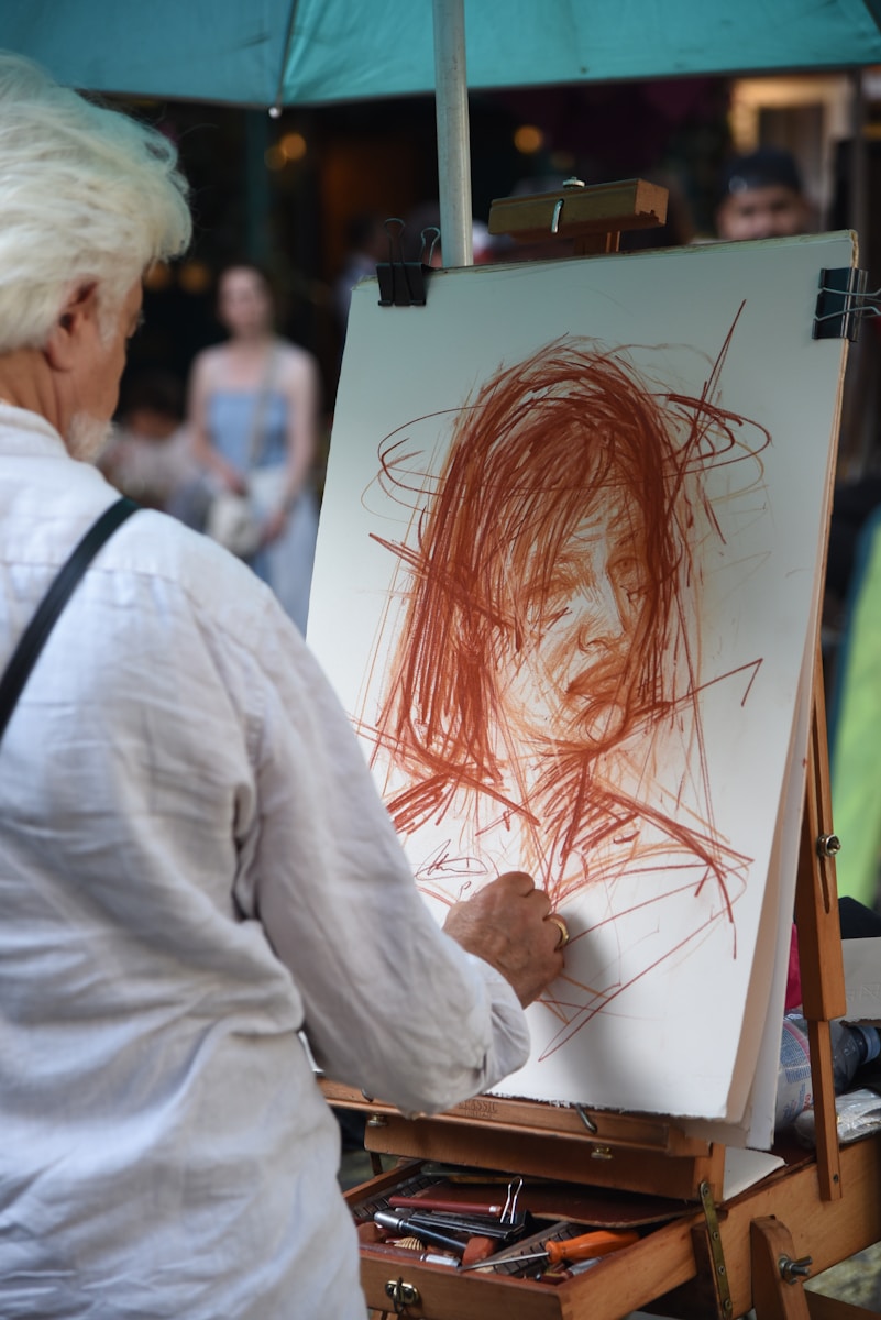 Artist sketching a portrait outdoors with easel.