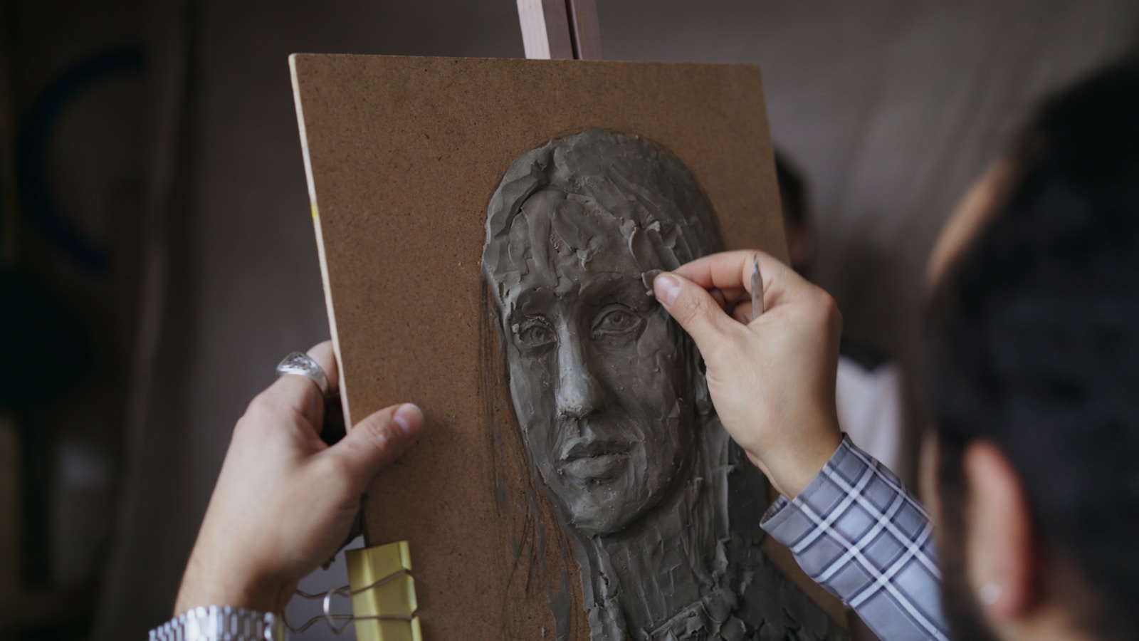 Artist sculpting a clay portrait on a wooden board